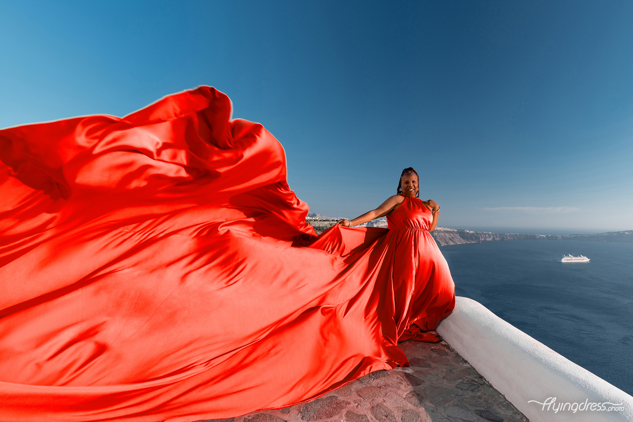 A stunning scarlet flying dress takes flight against Santorini's iconic caldera and deep blue Aegean sky.